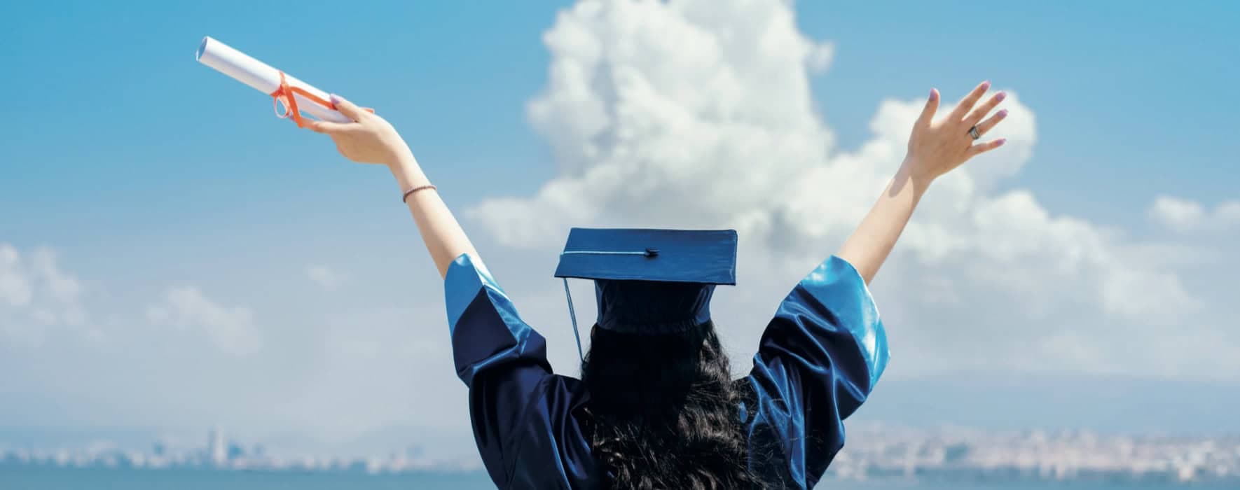 Graduate celebrating with arms raised against a city skyline